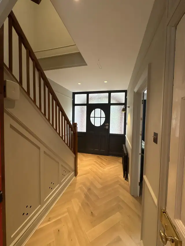 Hallway with painted stair panelling, white spindles and a herringbone floor
