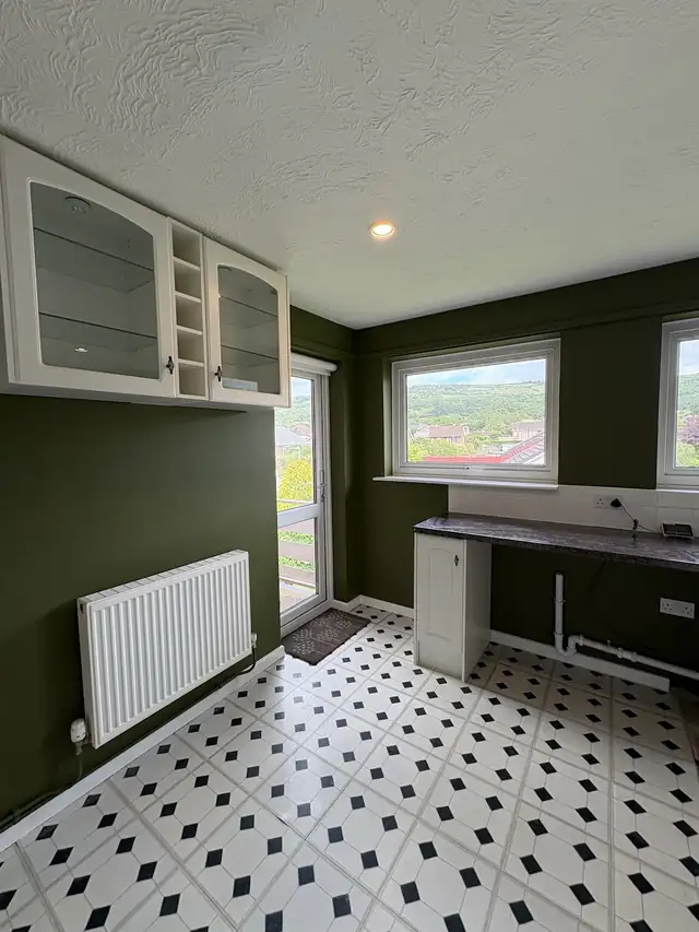 Kitchen with olive green walls, white wall cabinets and a patterned tiled floor