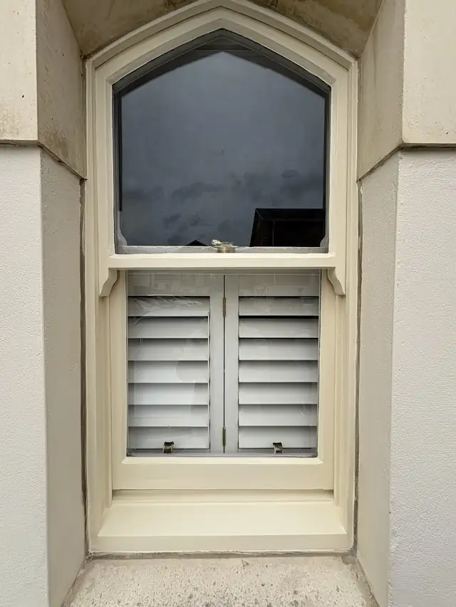 Cream painted sash window with shutters set in a stone surround